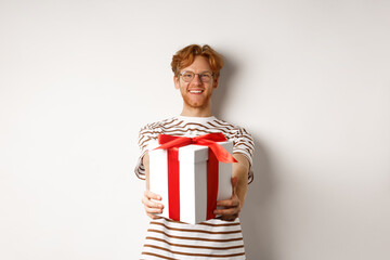 Wall Mural - Valentines day and holidays concept. Happy redhead man smiling and giving you gift box, congratulating with birthday, standing over white background