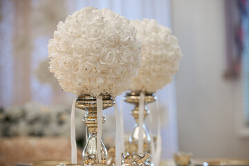 Wall Mural - Two white round faux flower in glass cylinder vase with silver base centerpiece at wedding reception table setting on white background close up