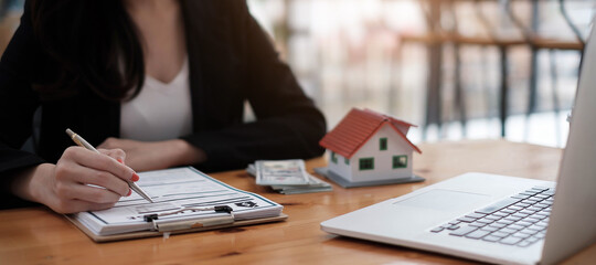 close-up view hands of businesswoman signing leasing home documents and have a house model on wooden desk