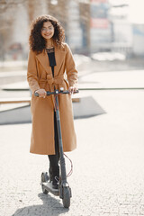 Wall Mural - Positive smiling woman riding a kick scooter