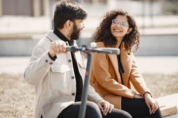 Wall Mural - Interracial young couple with scooters in the city background