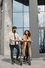 Wall Mural - Interracial young couple with scooters in the city background