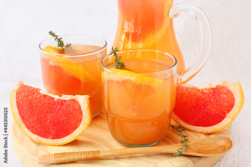Glasses and jug of tasty grapefruit juice on light background