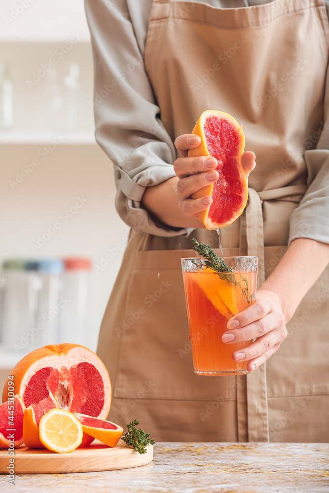 Woman squeezing grapefruit into glass in kitchen - obrazy, fototapety, plakaty 