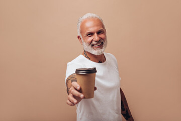 White haired man in T-shirt poses with tea cup. Smiling guy in light clothes with tattoos on his body holds coffee in his hand