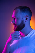 Close Up Portrait Of Young Caucasian Bearded Man Isolated On Dark Studio Background In Neon Lights. Side View