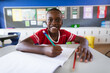 © WavebreakMediaMicro - Portrait of african american boy smiling while sitting on his desk in the class at elementary school