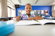© WavebreakMediaMicro - Portrait of african american girl smiling while sitting on her desk at elementary school