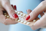 Fototapeta  - Woman with red manicure holding blister with contraceptive hormonal pills in her hands closeup