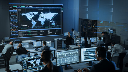 Wall Mural - Shot of Officers in a Surveillance Control Center with Police Global Map Tracking on a Big Digital Screen. Monitoring Room Employees Sit in Front of Computer Displays and Analyze Big Data.