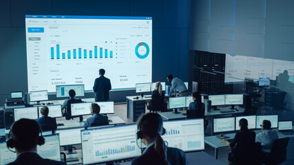 Wall Mural - Professional Traders Working in a Modern Monitoring Office with Live Analytics Feed on a Big Digital Screen. Monitoring Room with Brokers and Finance Specialists Sit in Front of Computers. 