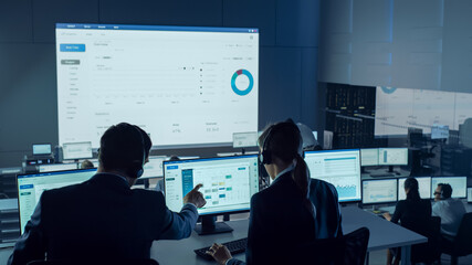 Fototapete - Professional Traders Working in a Modern Monitoring Office with Live Analytics Feed on a Big Digital Screen. Monitoring Room with Brokers and Finance Specialists Sit in Front of Computers. 