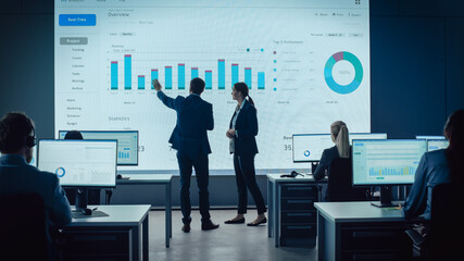 Fototapete - Two Traders Having a Meeting in a Modern Monitoring Office with Analytics Feed on a Big Digital Screen. Monitoring Room with Brokers and Finance Specialists Sit in Front of Computers. Colleagues Talk.