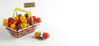 Horizontal banner with red and yellow cherry tomatoes in a shopping basket with an Organic Product sign. Side view on a white background. The concept of healthy and healthy nutrition.