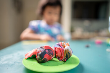 Wall Mural - Multicolor play dough on green plate against little girl at table.