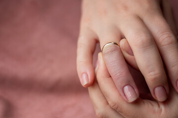 small gold wedding ring trying to remove from reddened finger with place for text on a pink background