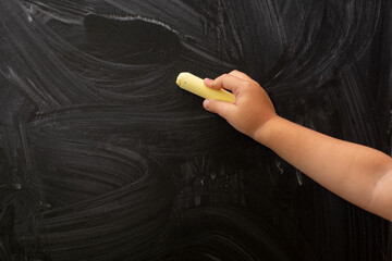 A child's hand holds chalk on a black chalk board.