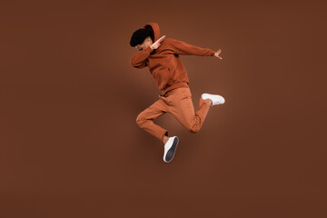 Wall Mural - Photo of pretty cool dark skin guy dressed hoodie humping high dancing showing dab sign isolated brown color background