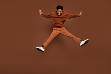 Wall Mural - Full size photo of cool yell short hairdo young guy jump dress sportswear trousers sneakers isolated on brown background