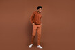 © deagreez - Full body photo of optimistic short hairdo young guy go dress sportswear trousers sneakers isolated on brown color background