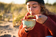 © Cavan Images - Young woman enjoying soup while beach car camping alone