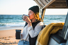 Young Woman Enjoying Drink In Mug While Beach Car Camping Alone