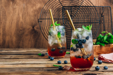 Wall Mural - Blueberry ice mojito with mint in tall glasses on rustic wooden background.