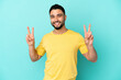 © luismolinero - Young arab man isolated on blue background showing victory sign with both hands