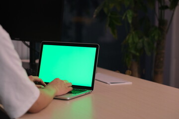 Wall Mural - over the shoulder view of people using green screen laptop computer on table in office at night