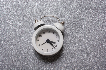 Sticker - Closeup of a white alarm clock on a gray glitter background