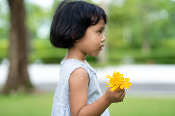 Wall Mural - Little Asian girl holding yellow flowers at field.