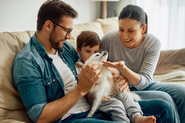 Wall Mural - Happy parents and their son enjoying while playing with their dog at home.