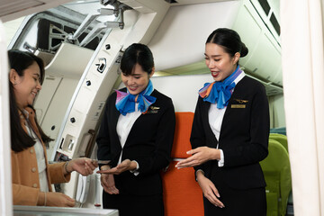 Two young beautiful Asian female flight attendants in suit uniform standing at the airplane entrance smiled friendly checking the Asian female passenger's boarding pass and welcoming her to the flight