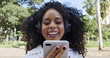 © Brastock Images - Young curly hair black woman walking using cell phone. Texting on street. Big city.
