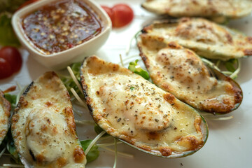 Plate of New Zealand mussels baked with cheese served on the table. Food close-up photo.