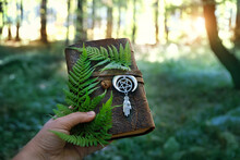 Magic Witch Book With Amulet And Fern Leaves In Hand On Natural Forest Background. Esoteric Ritual, Spiritual Practice. Mysticism, Divination, Modern Wicca Occultism Concept. Atmosphere Mystical Image