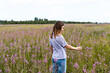 © Lena_viridis - Young beautiful smiling blond woman in purple shirt walking in meadow among flowers of fireweed and touching flower, beauty in nature landscape selective focus