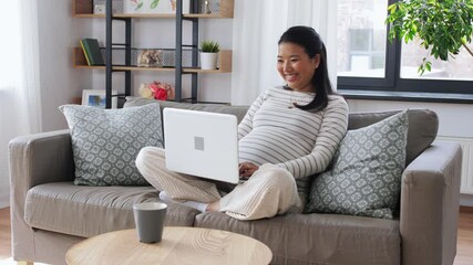 Wall Mural - pregnancy, rest, people and expectation concept - happy smiling pregnant asian woman with laptop computer sitting on sofa at home