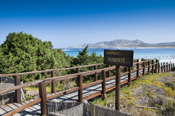 Wall Mural - Closeup shot of a sign and pier with Stintino comune in Sardinia, Italy in a distance