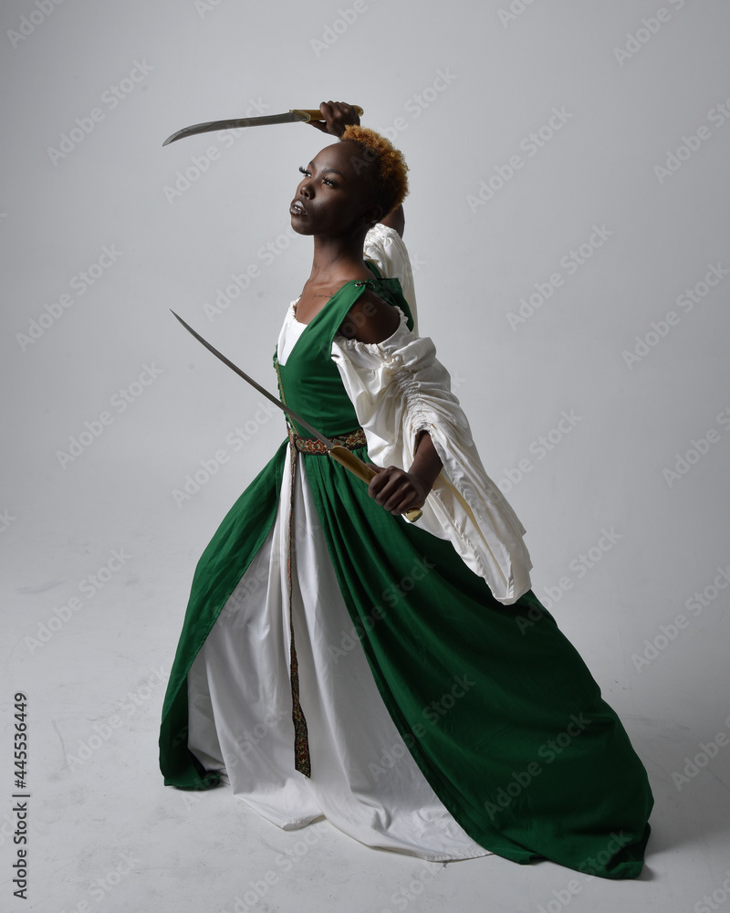 Photo Stock Full length portrait of pretty African woman wearing long green medieval fantasy gown holding sword, standing action pose on a light grey studio background. | Adobe Stock Photo Stock Full length portrait of pretty African woman wearing long green medieval fantasy gown holding sword, standing action pose on a light grey studio background. | Adobe Stock