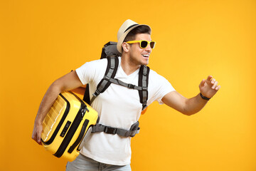 Poster - Male tourist with travel backpack and suitcase on yellow background