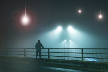 Wall Mural - A hooded figure, standing with back to camera on a bridge, looking at UFO alien spaceships coming down from the sky. On a foggy night.
