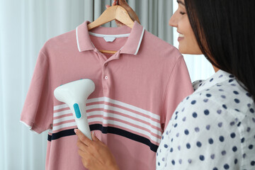 Wall Mural - Woman steaming shirt on hanger at home, closeup