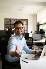 Young businessman using laptop in his office. Businessman offering hand for handshake