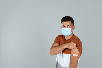 Canvas Print - Vaccinated man with protective mask showing medical plaster on his arm against grey background. Space for text