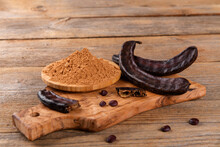 Dry Carob Pods And Carob Powder Over Wooden Background. Organic Healthy Ingredient For Vegan Vegetarian Food And Drinks, Close Up