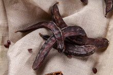 Dry Carob Pods On A Linen Nakpin Background. Organic Healthy Ingredient For Vegan Vegetarian Food And Drinks, Close Up