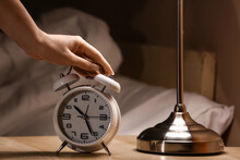Woman Turning Off Alarm Clock In Bedroom At Night, Closeup