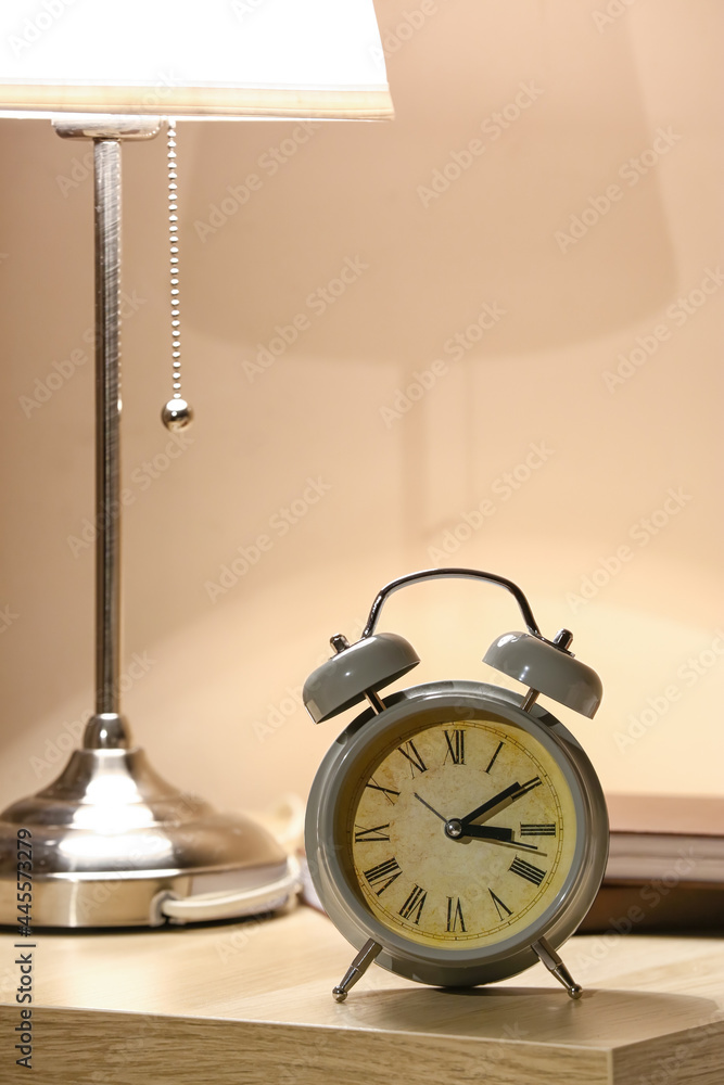 Alarm clock and glowing lamp on table in bedroom at night