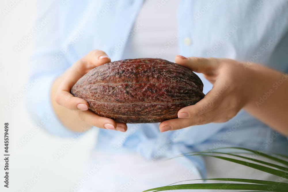 Woman holding fresh cocoa fruit on light background, closeup
